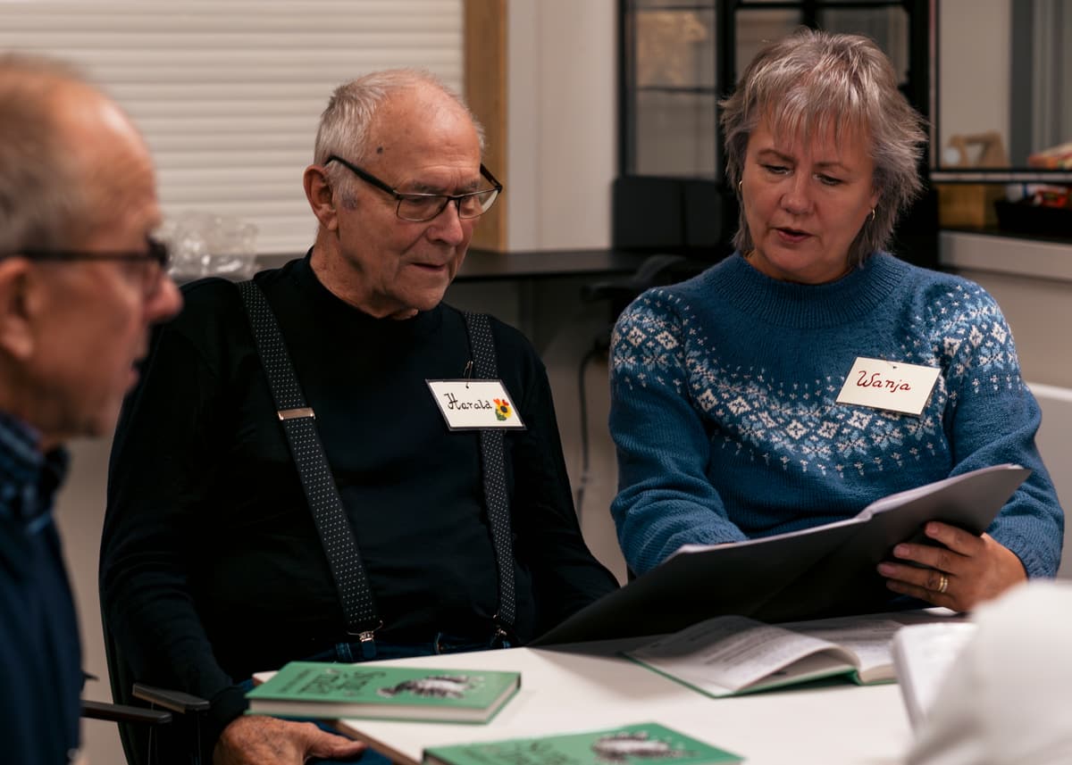 Konsentrerte sangere To eldre menn og en kvinne holder opp en sangperm og synger.