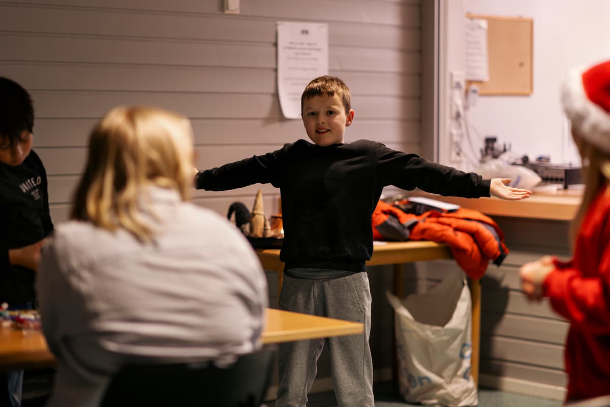 Glad gutt En smilende gutt slår ut med armene. Vi ser ryggen på to personer og en jente med nisselue.