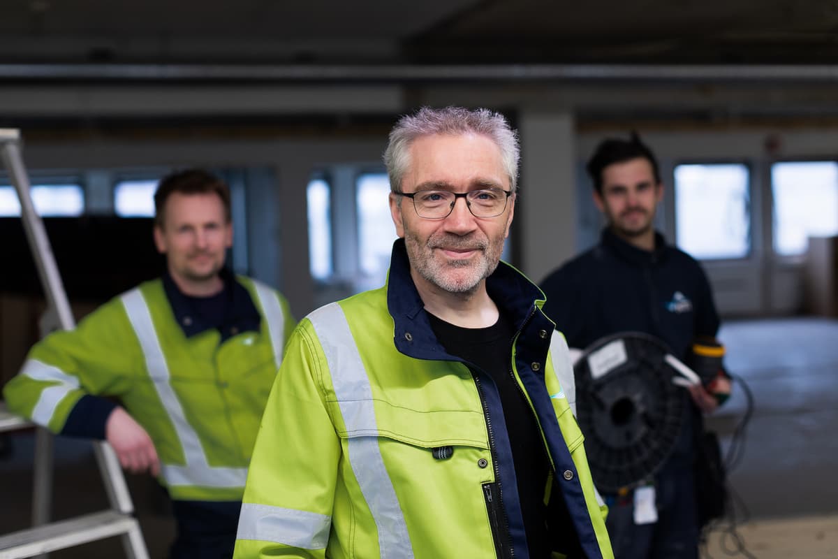Ketil Berg Mann i arbeidsjakke står foran to menn som holder verktøy i hendene