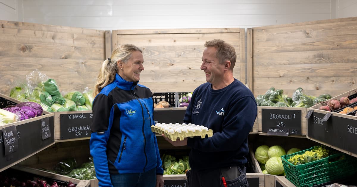 kari helga per ove Mann som holder et brett med egg smiler mot en dame på et kjølelager med grønnsaker