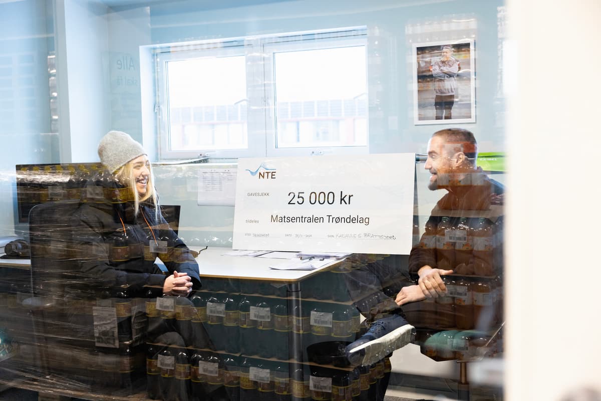 karianne brattgjerd og Jort Reitsma En mann og en kvinne i samtale. Mellom dem står en stor sjekk på 25 000 kroner til Matsentralen Trøndelag.