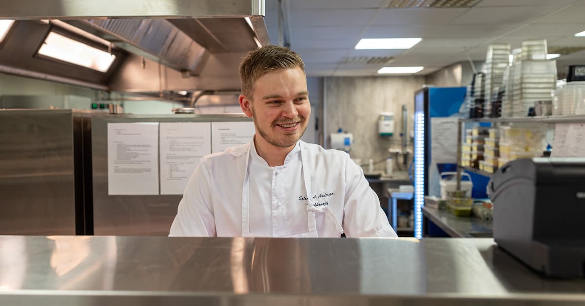 kokk kjøkken-kopi Mannlig kokk som smiler bak kjøkkenbenken