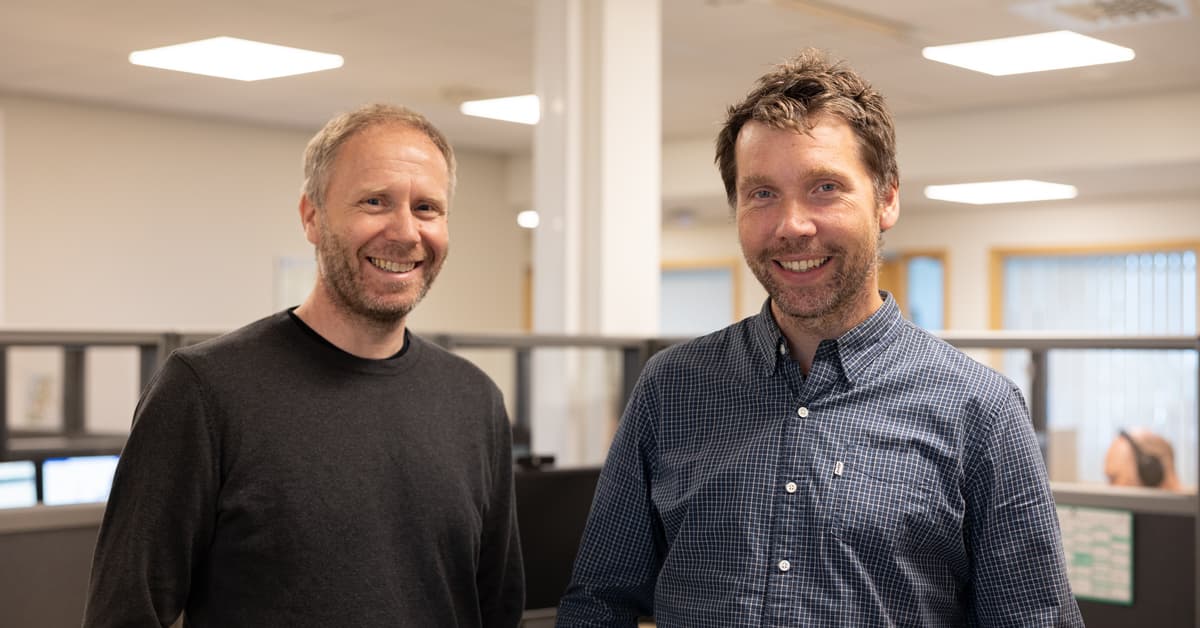 To smilende menn i et kontorlandskap To smilende menn i et kontorlandskap