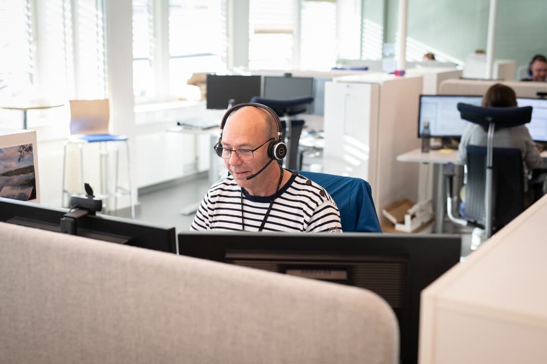 Kunderådgiver strøm og energi Bilde av en mann med headset som sitter bak to dataskjermer.