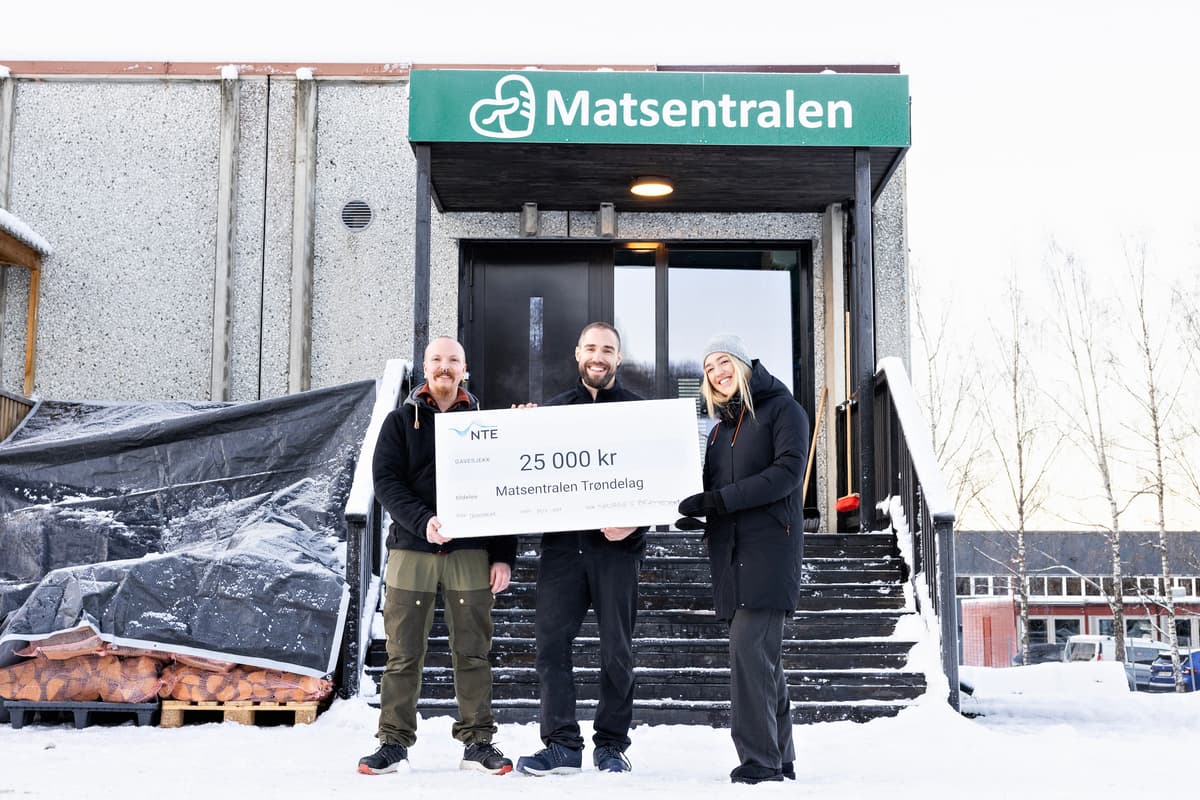 bilde med sjekken Tre mennesker holder en sjekk på 25 000 kroner mellom seg. De står under et skilt det står Matsentralen på.