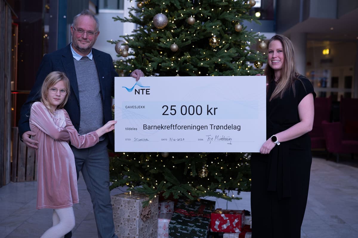 formell overrekkelse av sjekken Mann, kvinne og jente står foran et juletre og holder en sjekk på 25 000 kroner