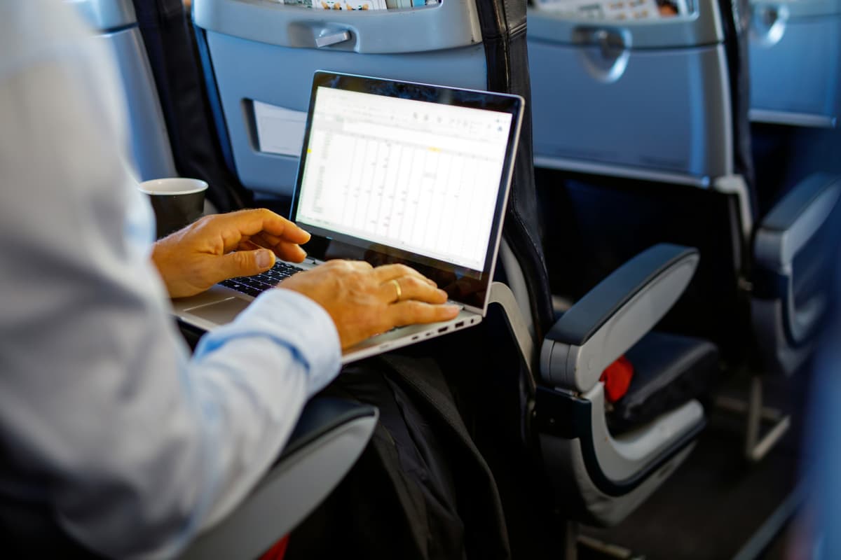 Sikker på reise Bilde som viser ryggen på en mann som sitter i et flysete med en bærbar PC.