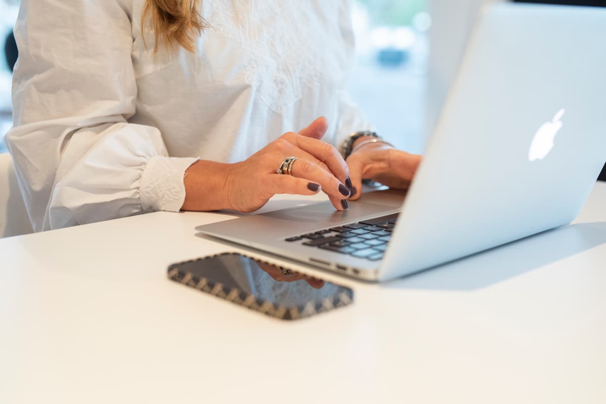 Kvinne som arbeider Hjemmekontor Hendene og overkroppen til en kvinne som jobber på en Mac. Ved siden av ligger en telefon.