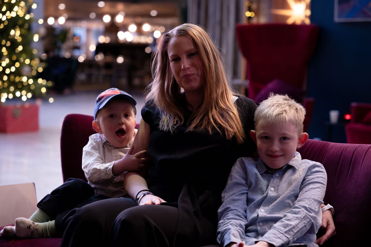 rikke med guttene Mor og to sønner sitter sammen i en sofa foran et juletre