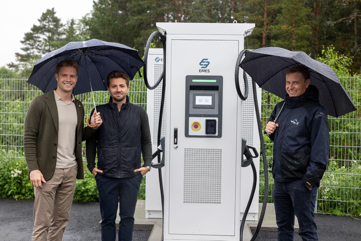 Børstad og NTE ved ladeanlegget Tre smilende menn, to av dem med paraply, står ved siden av et ladeanlegg