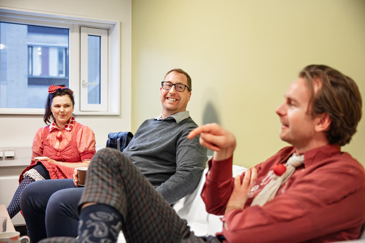 samtale mellom klovner En kvinne og to menn sitter i en sofa og snakker sammen.